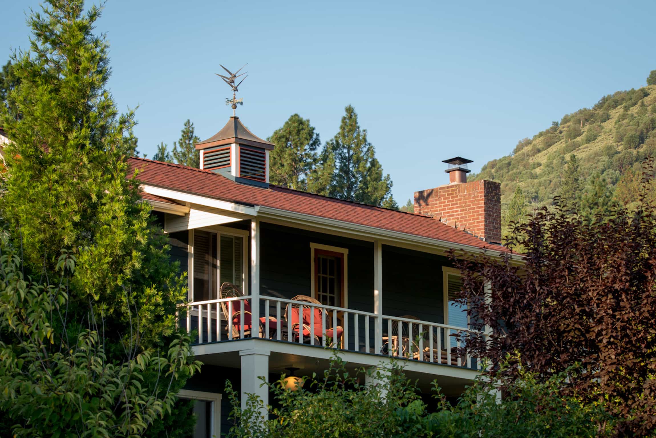 A view of Country Willows Inn & Estate in Ashland, Oregon, nestled on the mountainside, with comfortable covered porches overlooking the gardens.